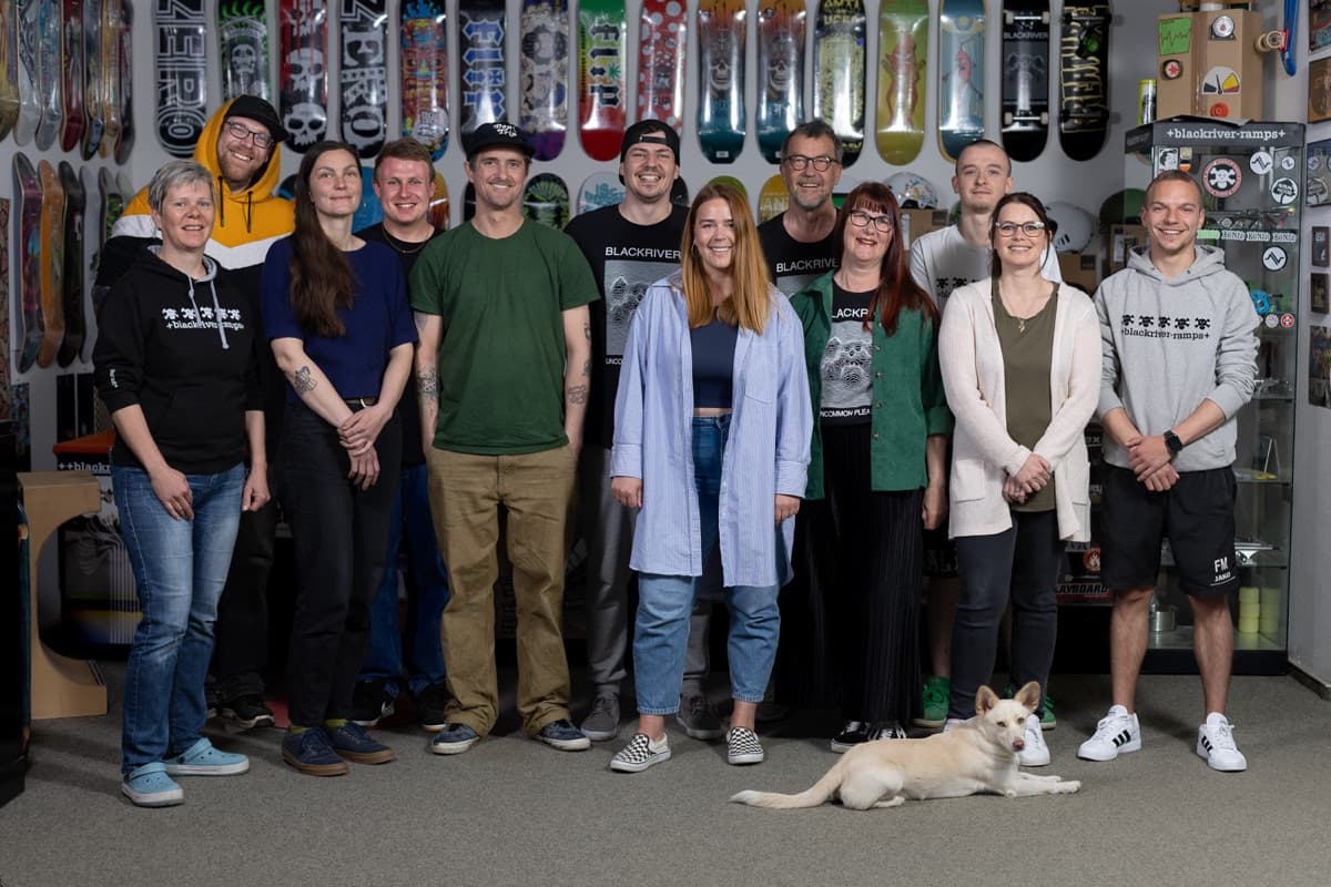 The Blackriver team standing in their shop in front of a wall of skateboard decks, with a dog resting in front, from the brand's official about page.