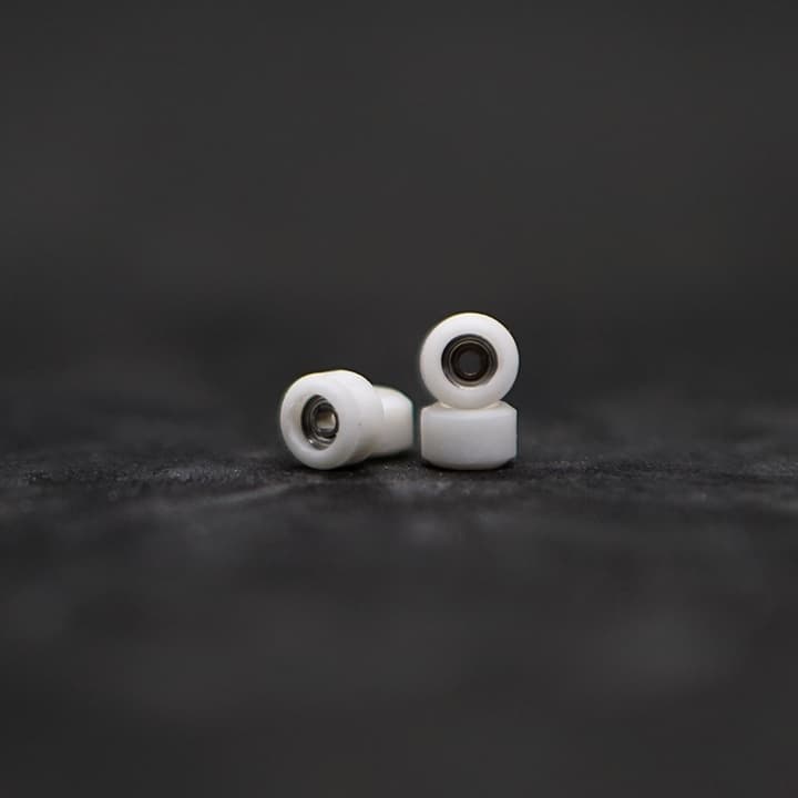 A pair of Oak white urethane OG-shape fingerboard wheels with bearings on a dark surface, from the official Oak Wheels storefront.