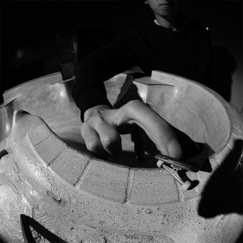 A rider fingerboarding the tiled coping of a concrete bowl, photographed in dramatic black and white.