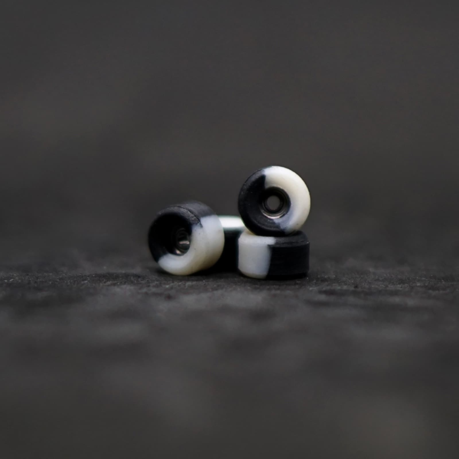 Black and white split urethane fingerboard wheels stacked on a dark surface, macro shot.
