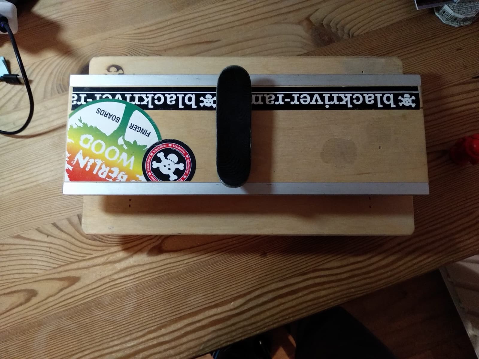 A wooden fingerboard resting on a small picnic-table obstacle on a desk.