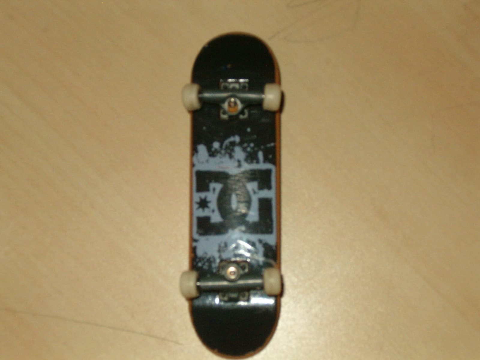 A fingerboarder outdoors holding up a yellow wooden fingerboard, smiling.