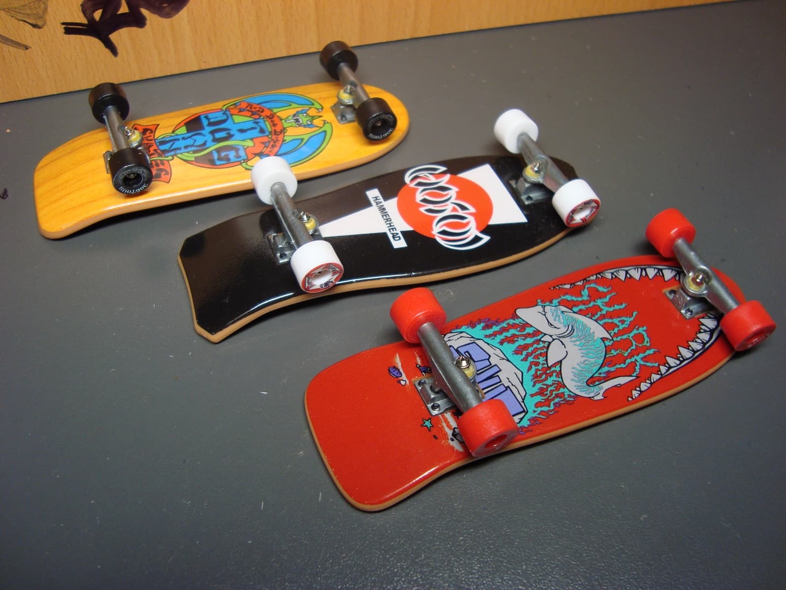 Three vintage-style wooden fingerboards with old-school deck shapes and hand-drawn graphics.