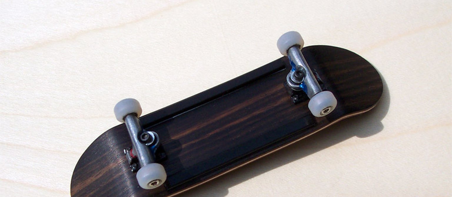 A plain wooden fingerboard with white wheels on a light tabletop.