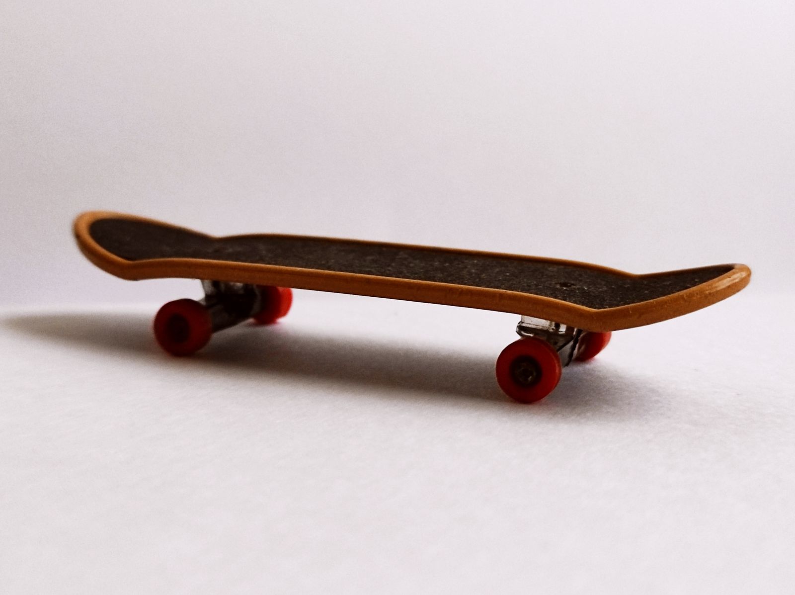 Side profile of a wooden fingerboard with bright red wheels on a white background.