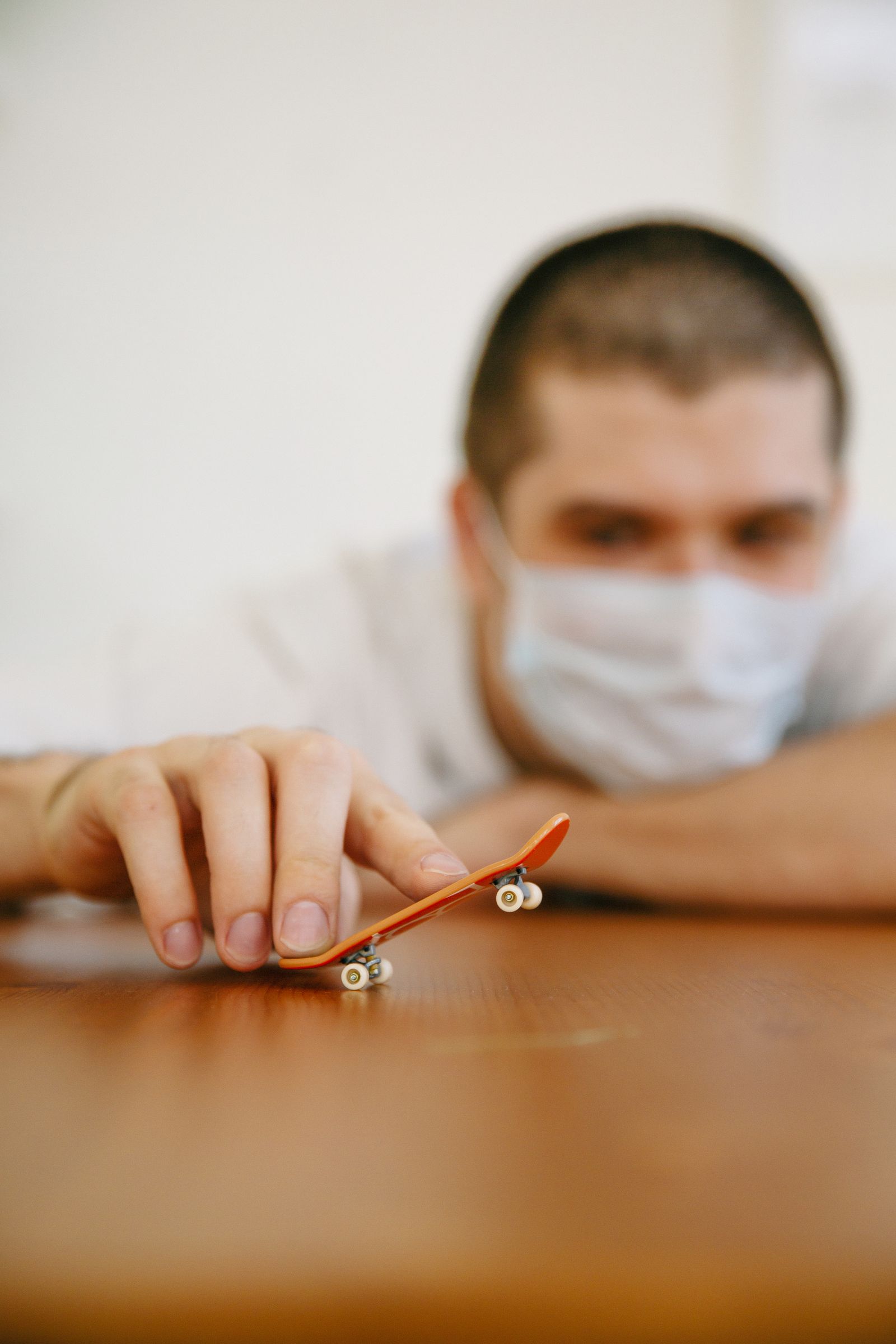 A person riding an orange fingerboard across a wooden floor, shallow depth of field.