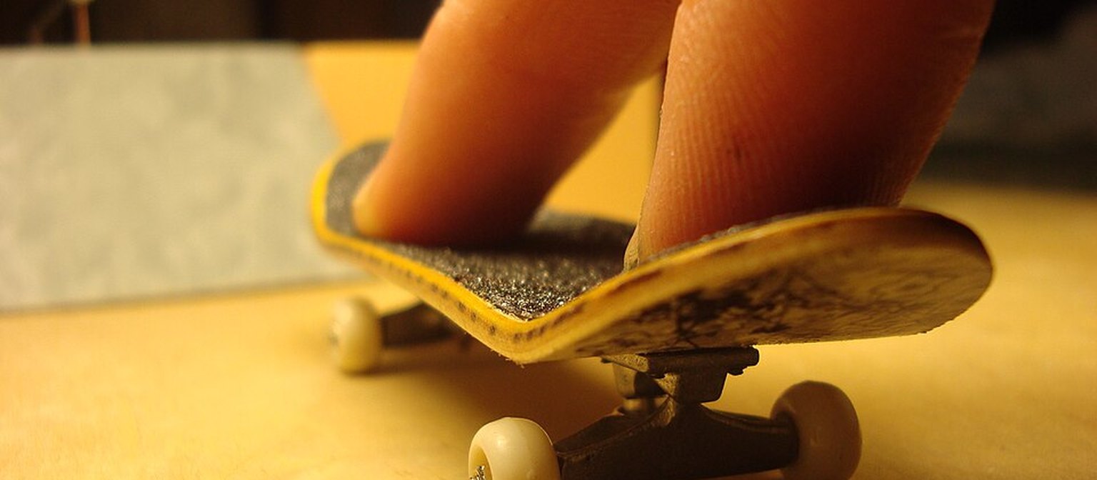 A close-up of a wooden fingerboard flexing on its truck and white wheels.