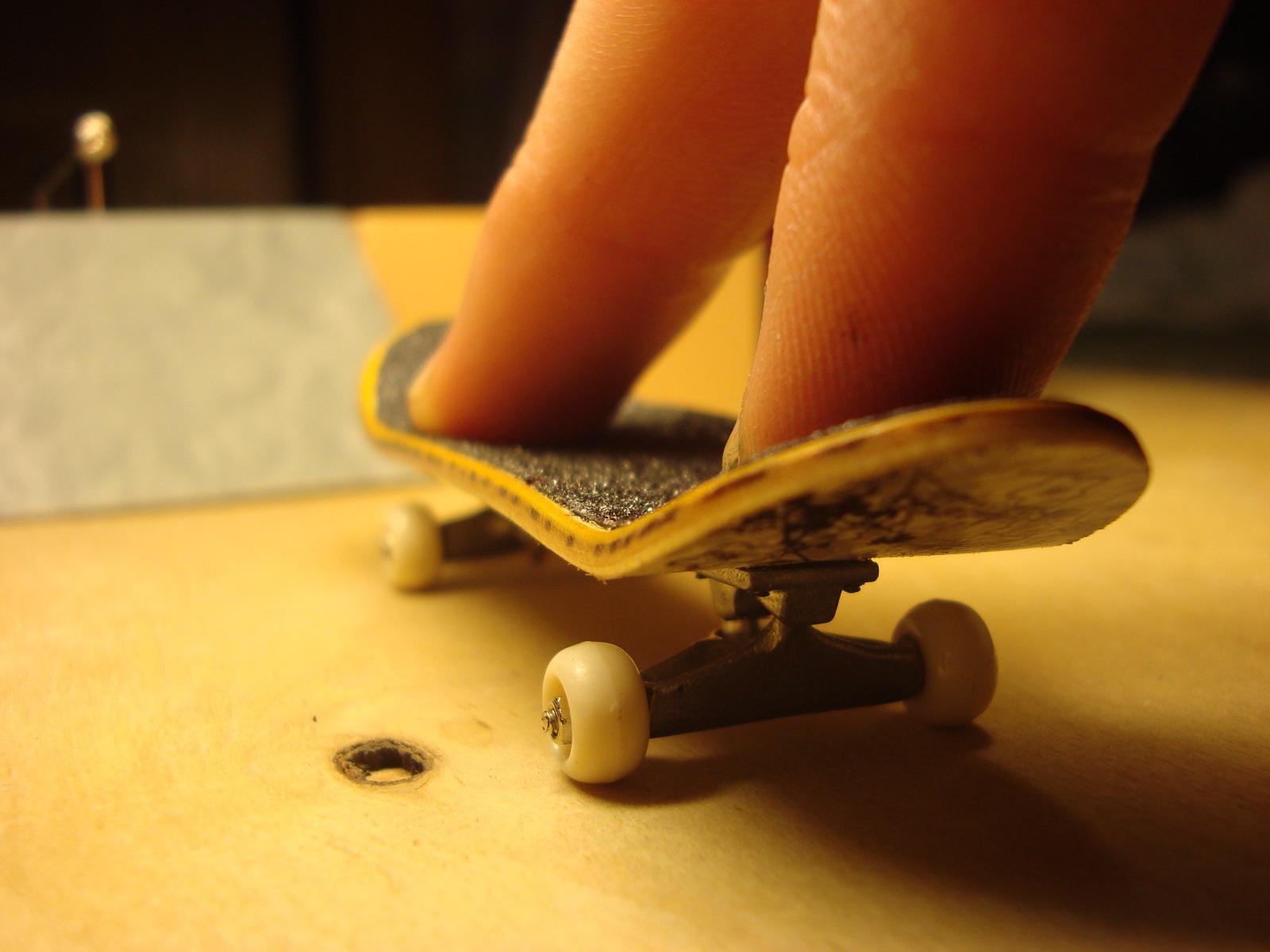 Close-up of a finger riding an assembled wooden fingerboard with white wheels.